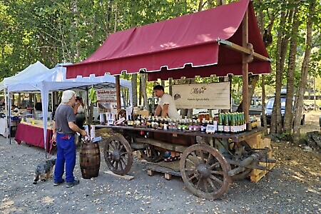 Banco espositivo allestito su un antico carro in legno con bottiglie, vasetti e prodotti agricoli artigianali, lungo il percorso della Mostra Mercato.